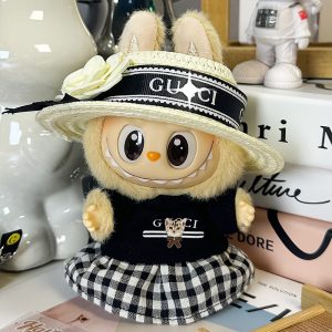 Labubu rayonne d’élégance dans cette tenue campagne-chic ! Vêtue d'une robe à carreaux vichy noir et blanc, ornée d'un haut noir brodé "Gucci" avec motif tigre raffiné, cette figurine allie douceur et style. Le tout est sublimé par un superbe chapeau en paille avec ruban Gucci noir et fleur blanche en tissu. Un véritable bijou de collection à l’esprit raffiné et printanier.